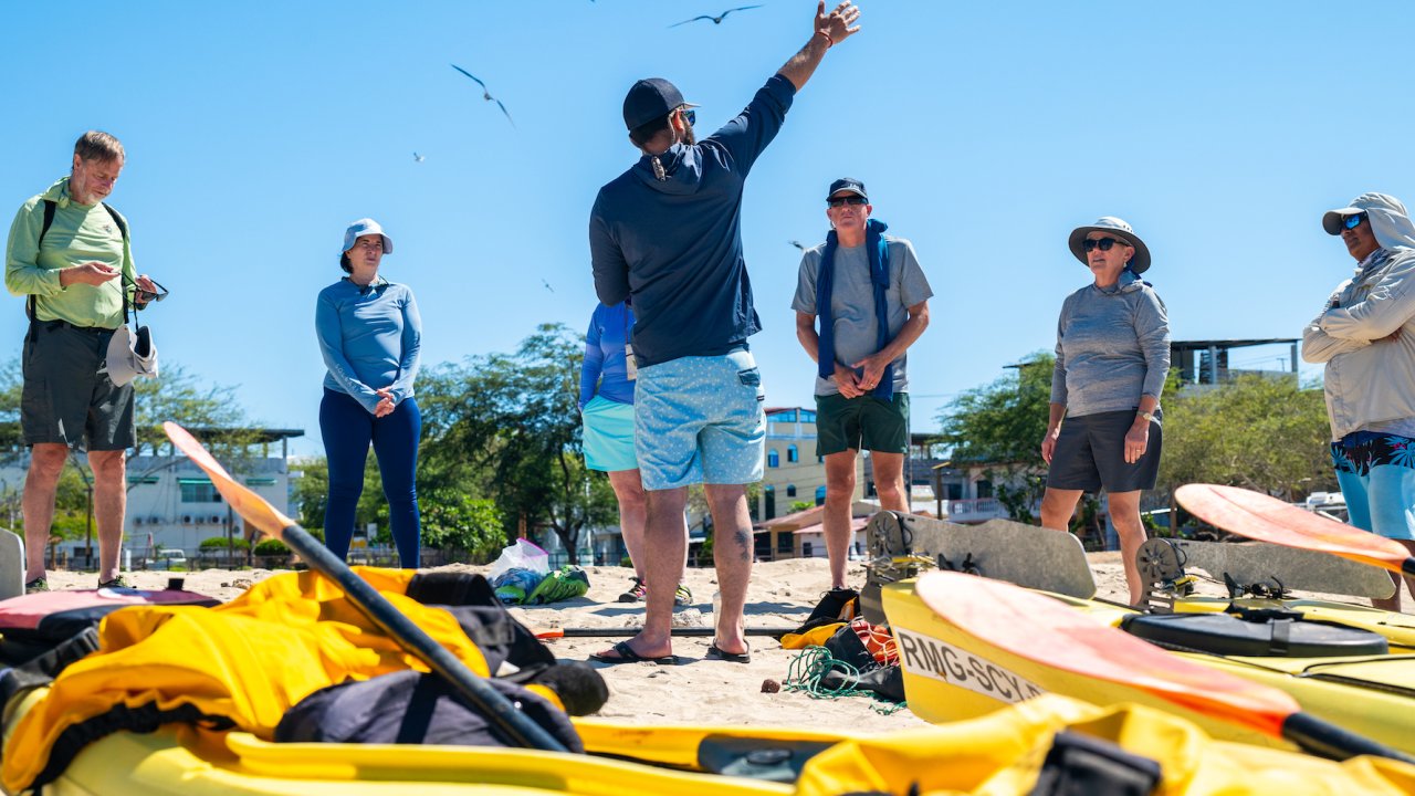 A local Galapagos tour guide talking to a group of sea kayakers before their paddling journey on a sunny day