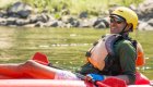 Man in a red inflatable kayak wearing a yellow helmet smiling on the Salmon River