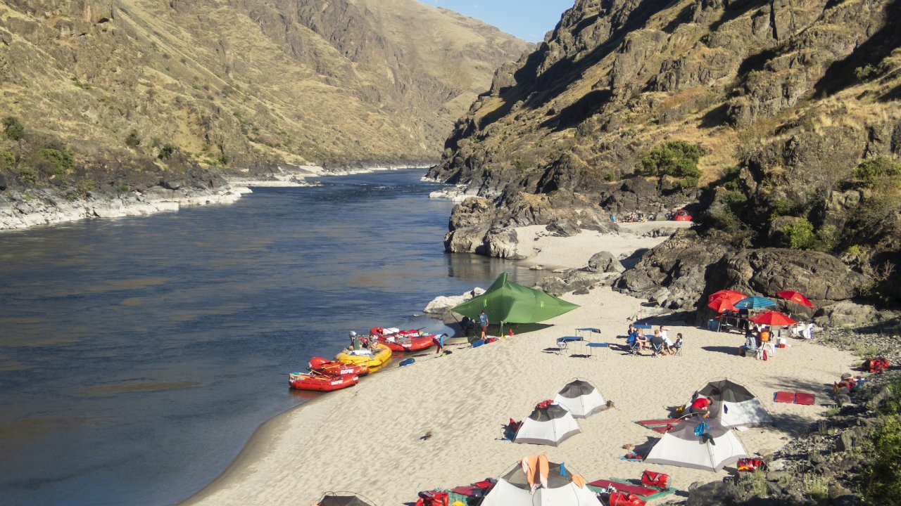 Tents and other gear sprawled out on a white sand beach in the middle of a multi-day rafting trip down the Snake River through Hells Canyon