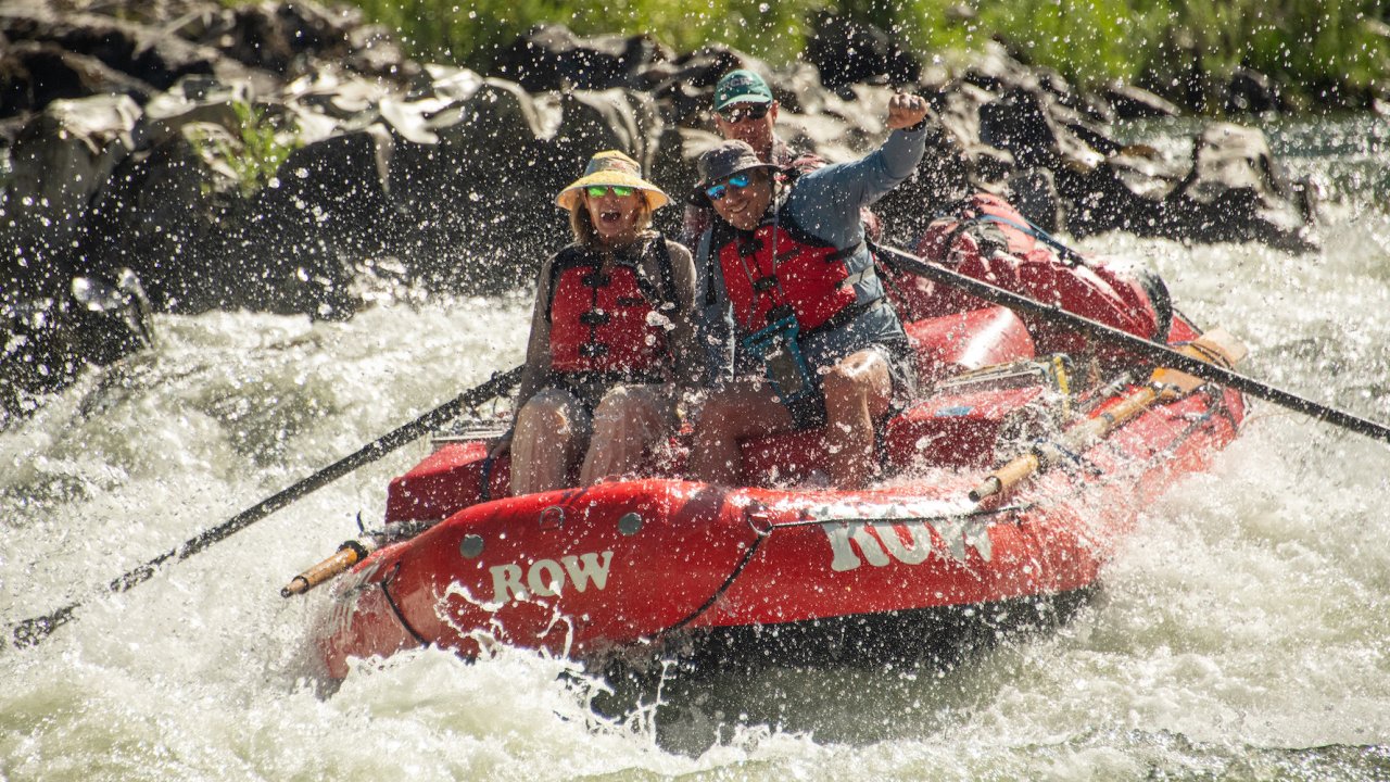 A couple on the bow of a red raft as a guide rows them through a rapid on the Rogue River