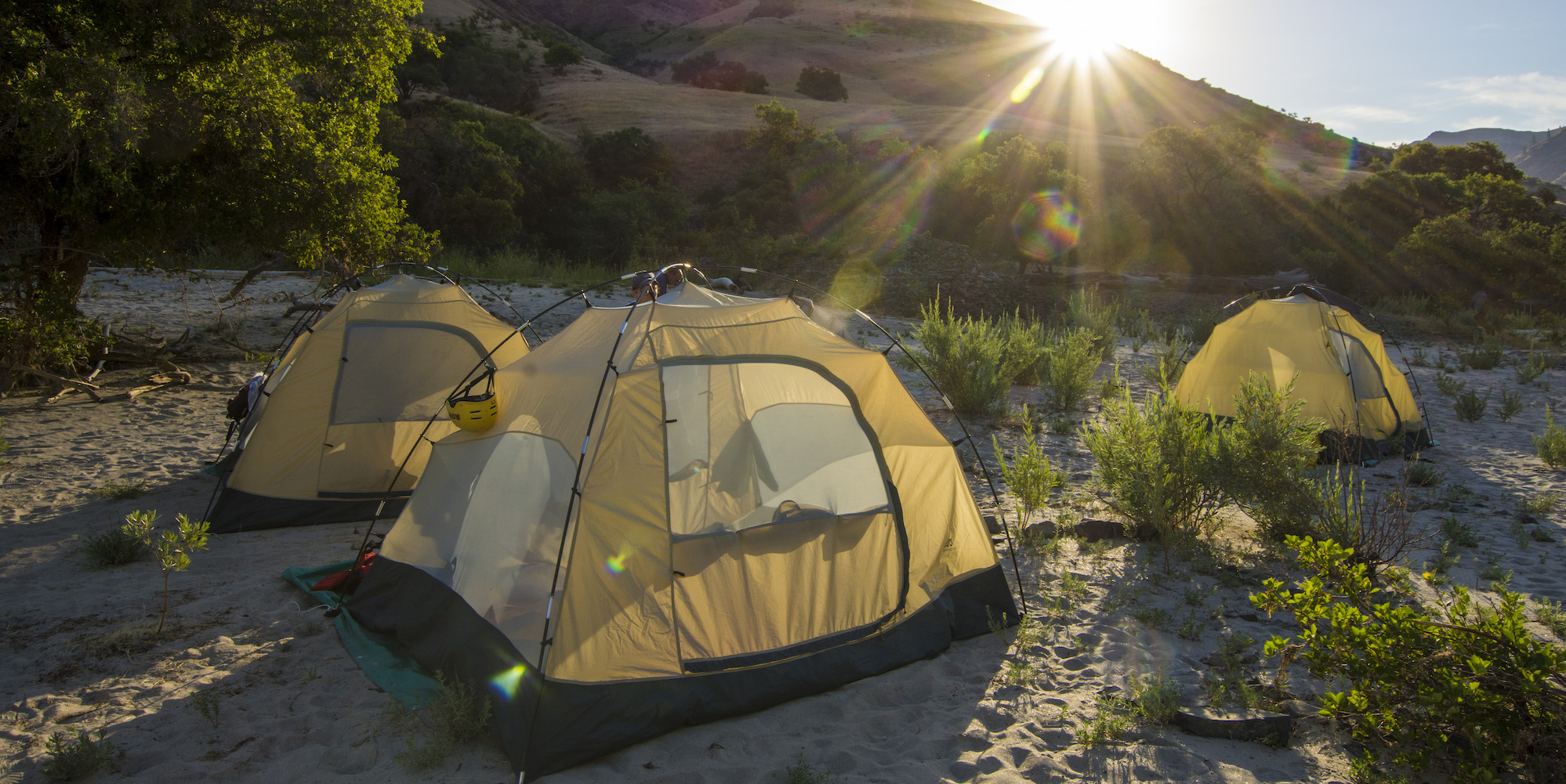 Three tents set up in the sand as the sunrises over them