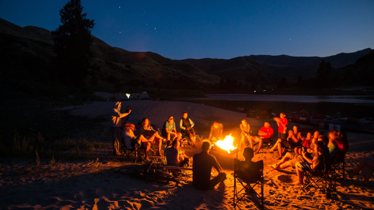 Group of people around a campfire on a sandy beach along a river in Idaho