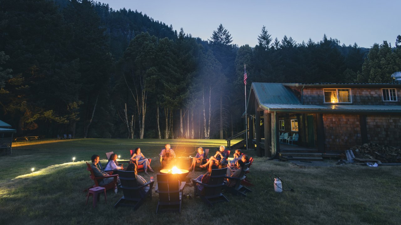 A group of whitewater rafters gathered around a campfire at Half Moon Bar Lodge in Oregon