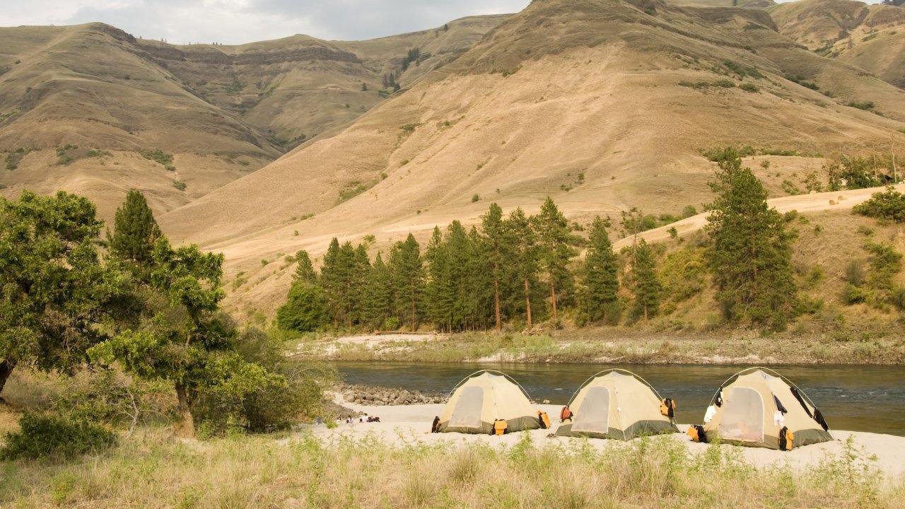 Tents set up on a sandy riverbank surrounded by Idaho hills.