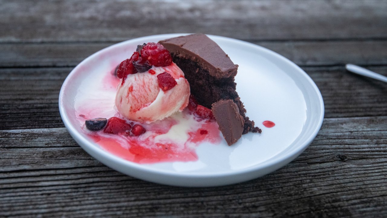A slide of chocolate cake with vanilla ice cream and raspberries on a white plate
