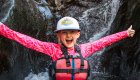 A young girl sitting at the base of a small waterfall and smiling while on a ROW Adventures family rafting trip in Idaho.