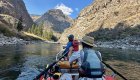 The back of a whitewater raft guide rowing a guest fishing at the front of the boat on the Middle Fork Salmon River