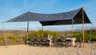 A big wind fly set up over a long table with camp chairs on a beach