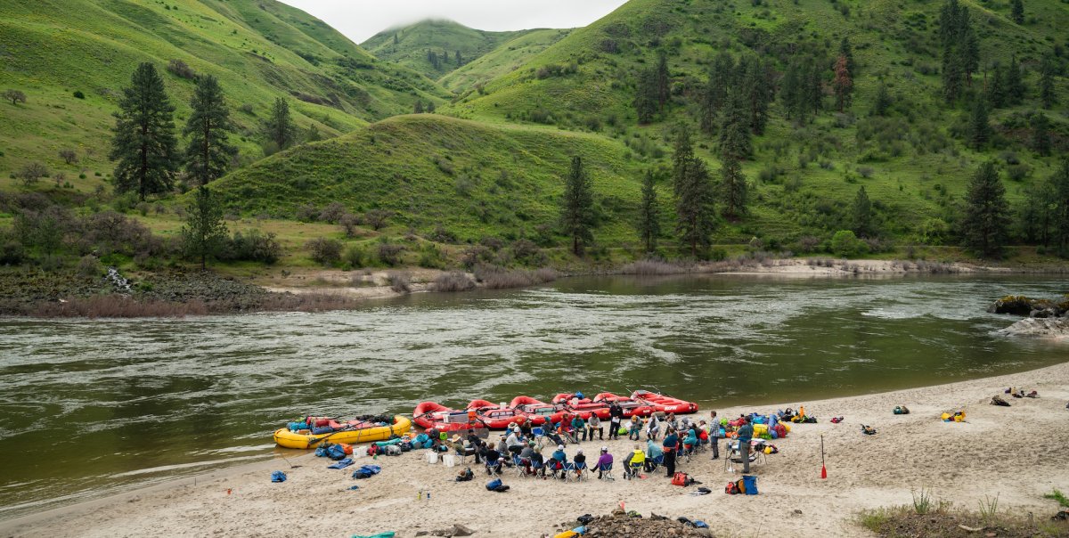 Group of whitewater rafters sitting in a circle on a sandy beach along the river