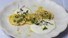 A plate of gourmet ravioli topped with greens, olive oil, and served with a white sauce. 