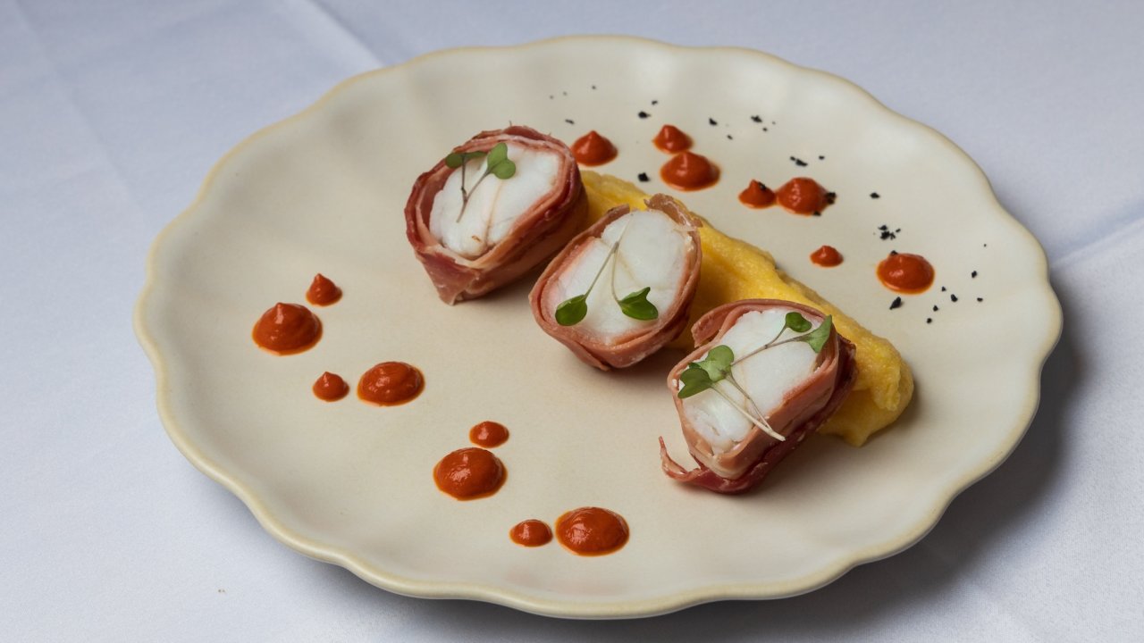 Gourmet dish plated on a cream colored plate with a red sauce drizzled on top.