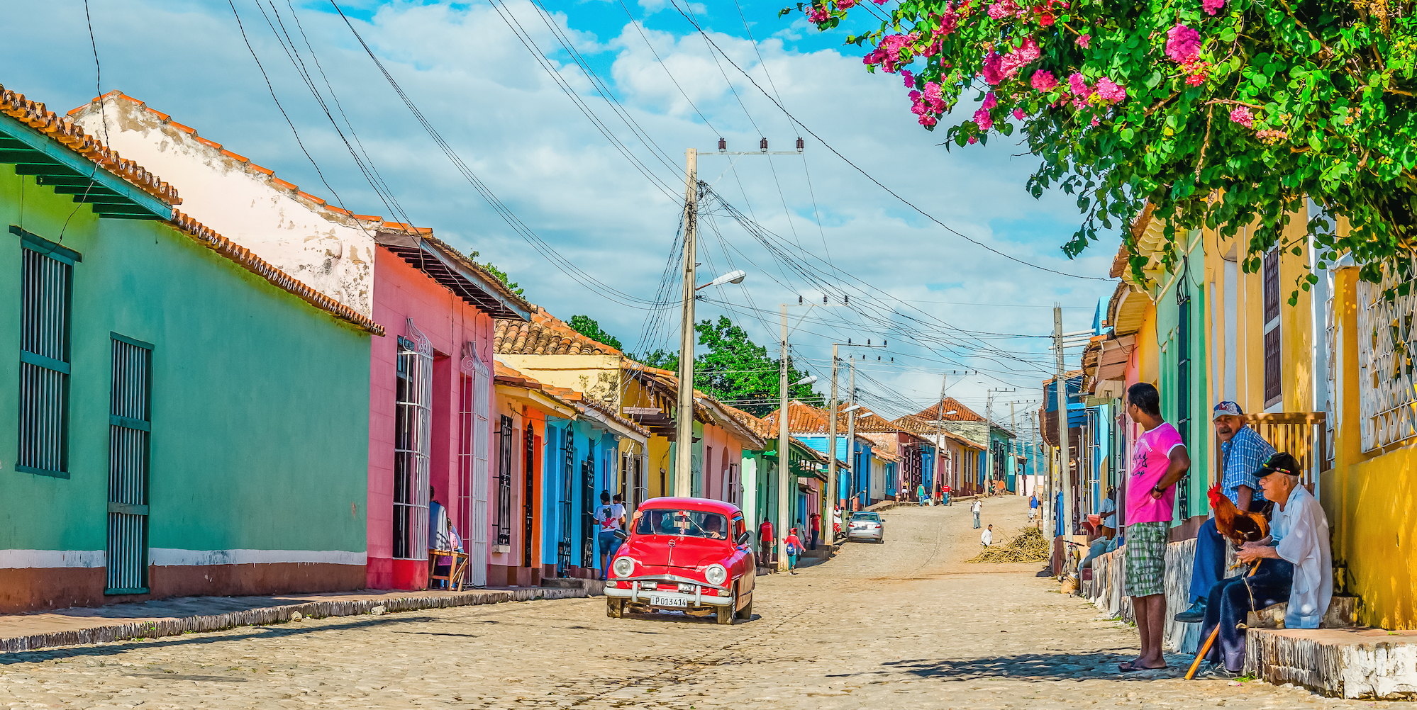 Three men in the right hand corner with one holding a chicken looking over the cobblestone roads of colorful Cuba