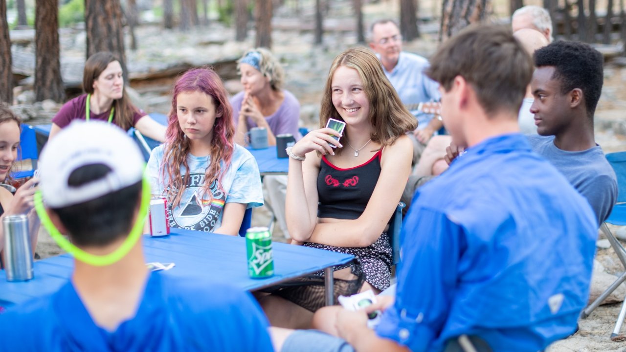 Group of teens and adults playing cards at a campsite.