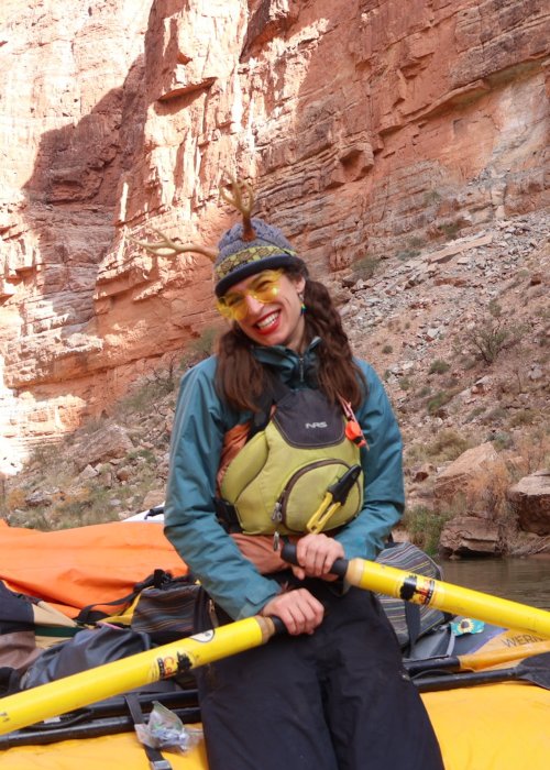 ROW Adventures guide Jade sitting on a yellow boat with oars in her hands.