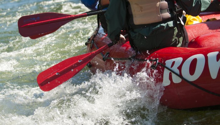 A red ROW raft floating over a splashy section of river