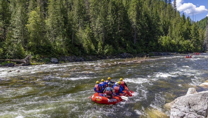 A red raft full of people dressed in rain gear and life jackets floating downstream. 
