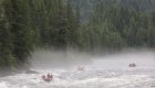Downstream shot of two red rafts floating down the Lochsa River among dense forests on a cloudy day