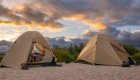 Two double tents with rain flies set up on a beach at sundown