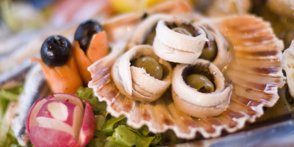 Marinated anchovies with green olives on a sea shell looking plate
