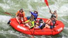 A red ROW branded raft full of people holding red and black paddles with the guide in the back holding their paddle up in the air