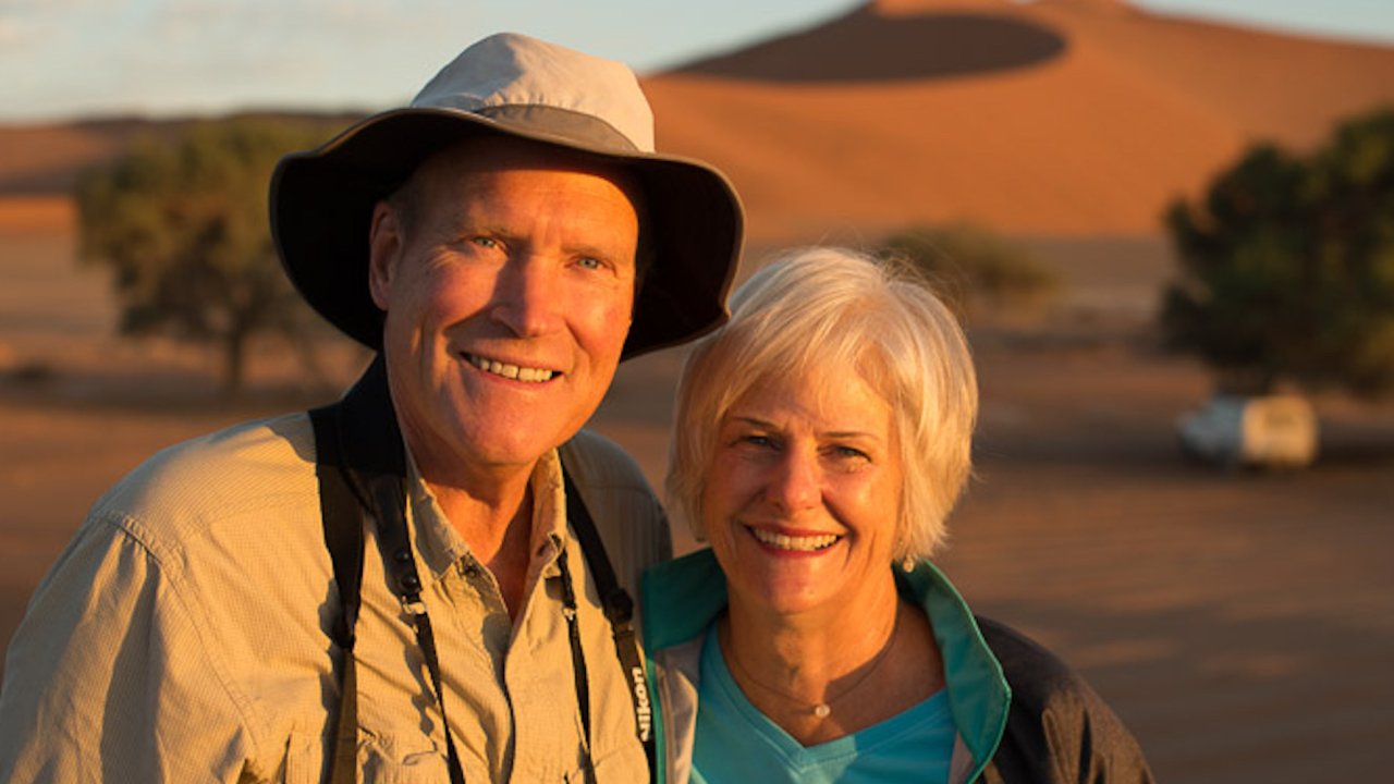 A man on the left and woman on the right smiling while on safari in Africa at sunset