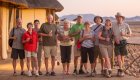 A group of safari travelers in Africa standing on a wooden deck next to their canvas style tent lodges 