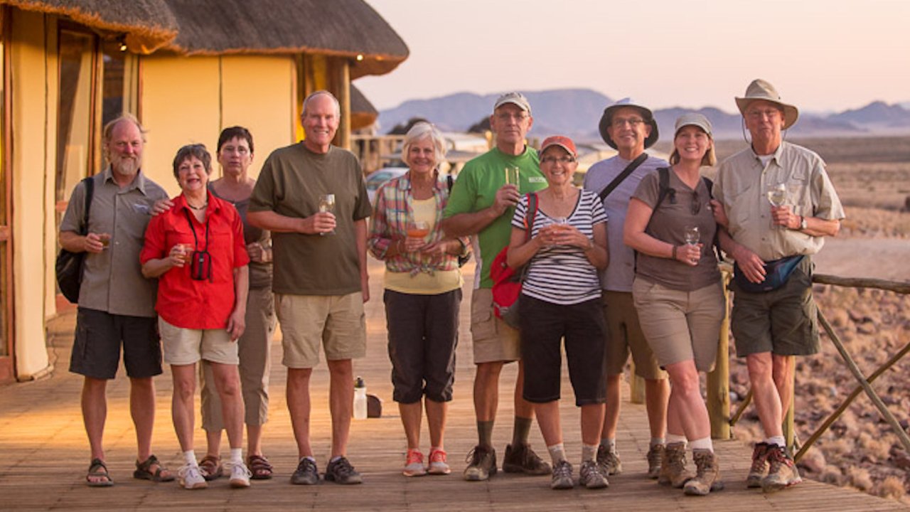A group of safari travelers in Africa standing on a wooden deck next to their canvas style tent lodges