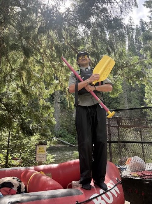 ROW Adventures river guide standing on top of a red ROW raft holding a broken red and yellow paddle