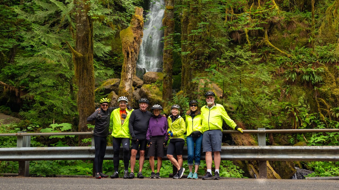 A group of bikers stop for a photo in front of a waterfall in Olympic National Park