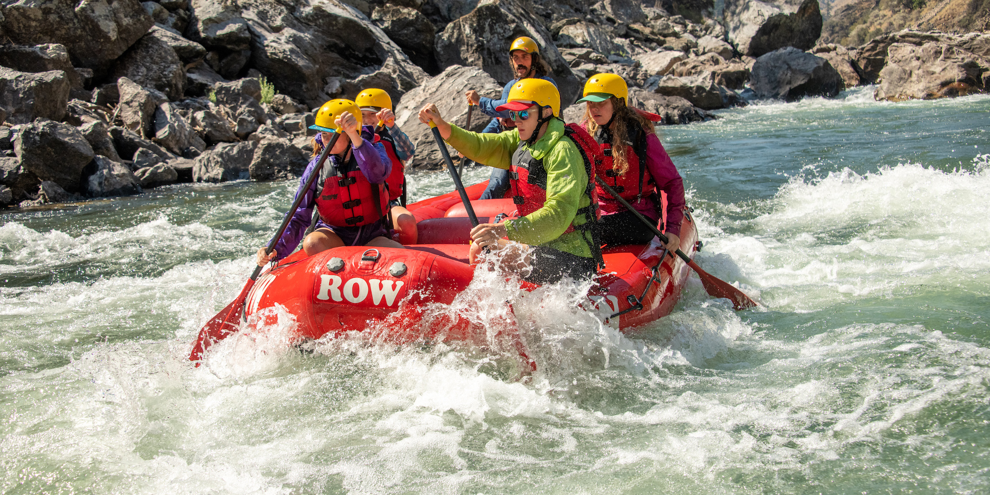 A group of people on a red raft paddling through a rapid on a sunny day