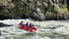 Side view of a red raft in a whitewater rapid with a large rock wall behind it