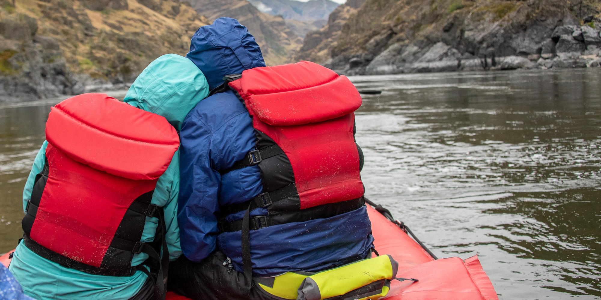 Two people wearing raincoats while on a whitewater rafting trip. 