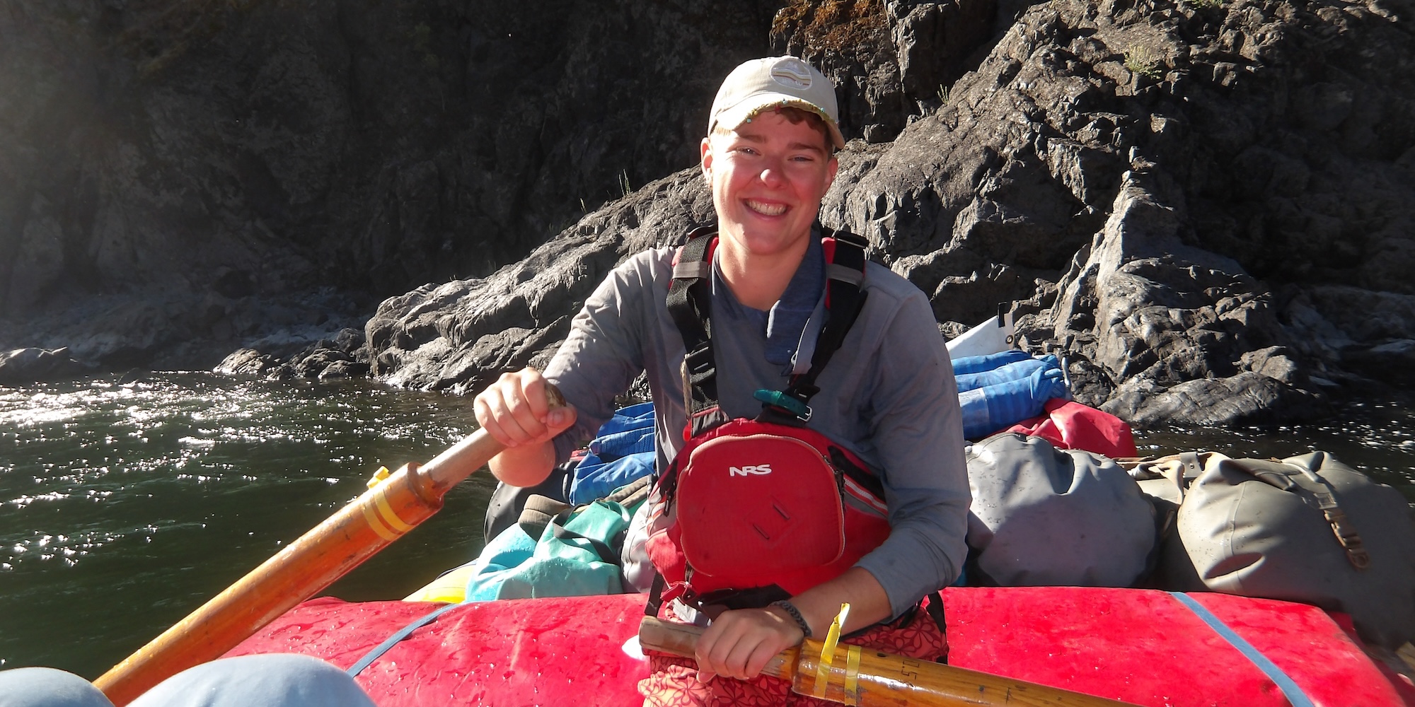 ROW Adventures raft guide smiling while navigating a raft downstream. 