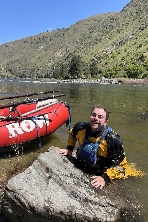 ROW River guide in the river near a red raft.