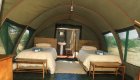 The inside of a canvas style tent with two twin beds and a small bathroom in the back in Namibia