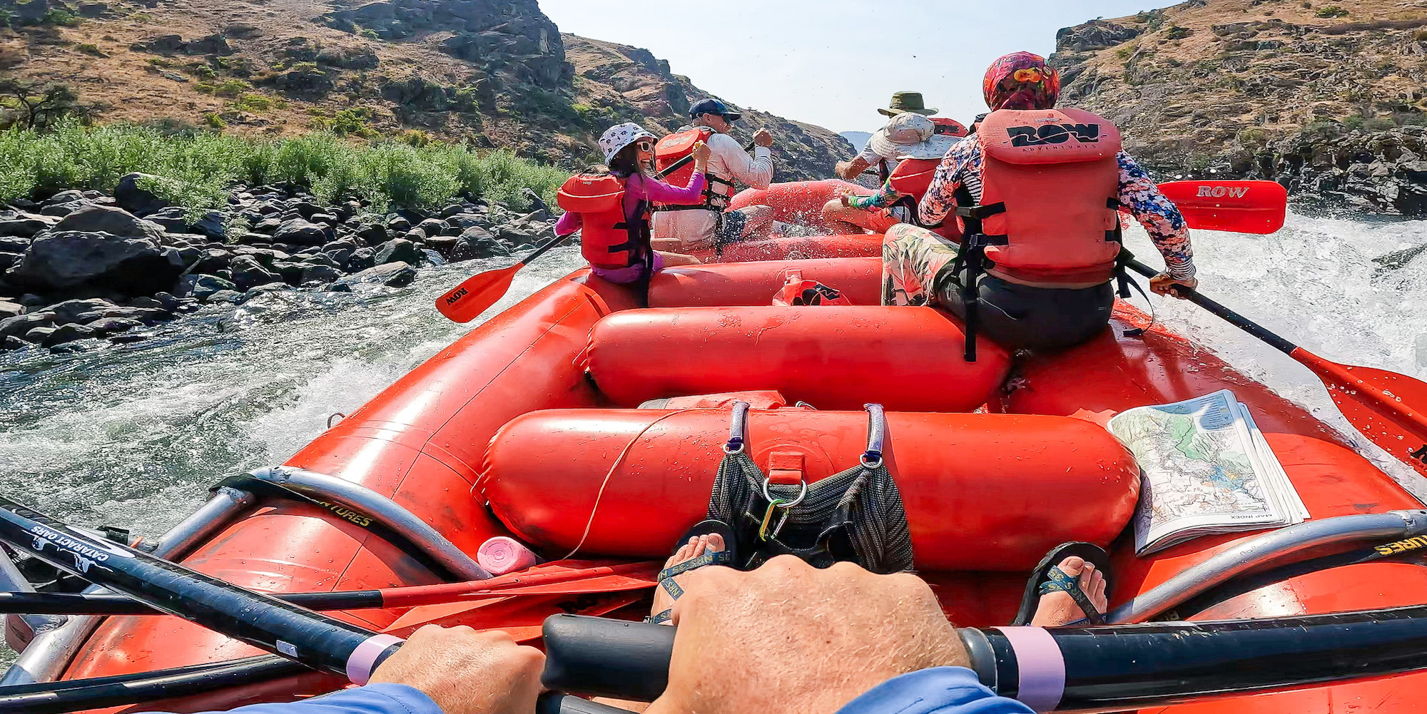 Guide POV rowing a boat through a rapid with paddlers up front