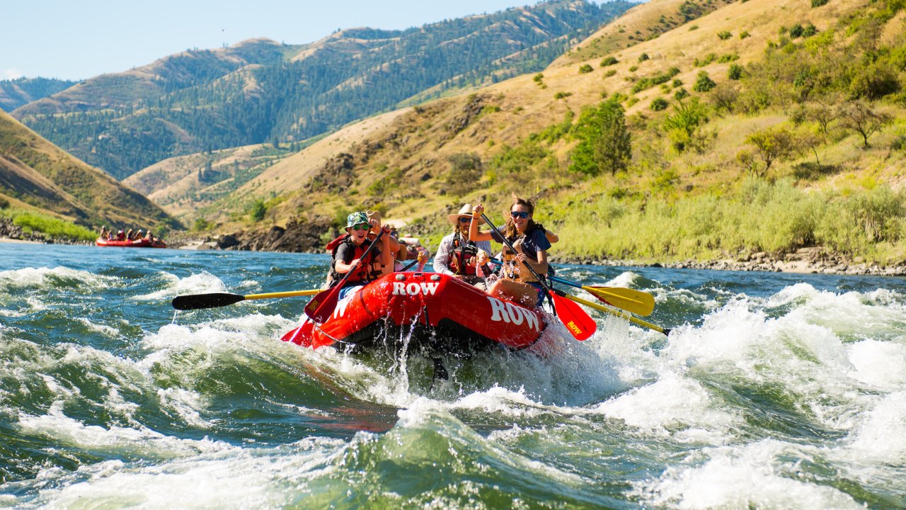 Red raft full of paddlers going through a rapid on the Salmon River Canyons on a sunny and warm day