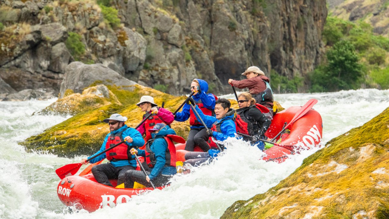 Hillary threads the needle on the Snake River in Idaho. red whitewater raft with paddlers passing through large rocks on river