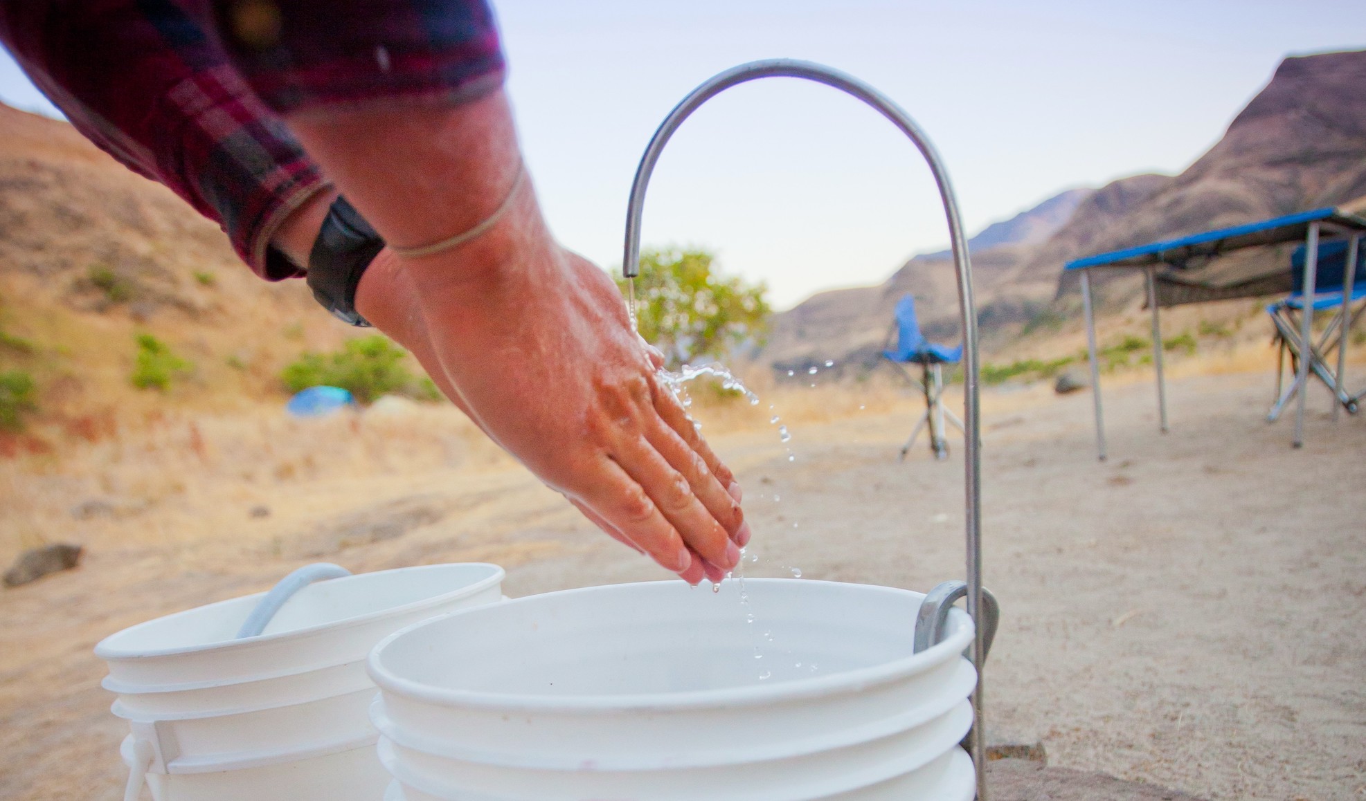 Woman washing her hands in buckets while camping on the river in the Pacific Northwest