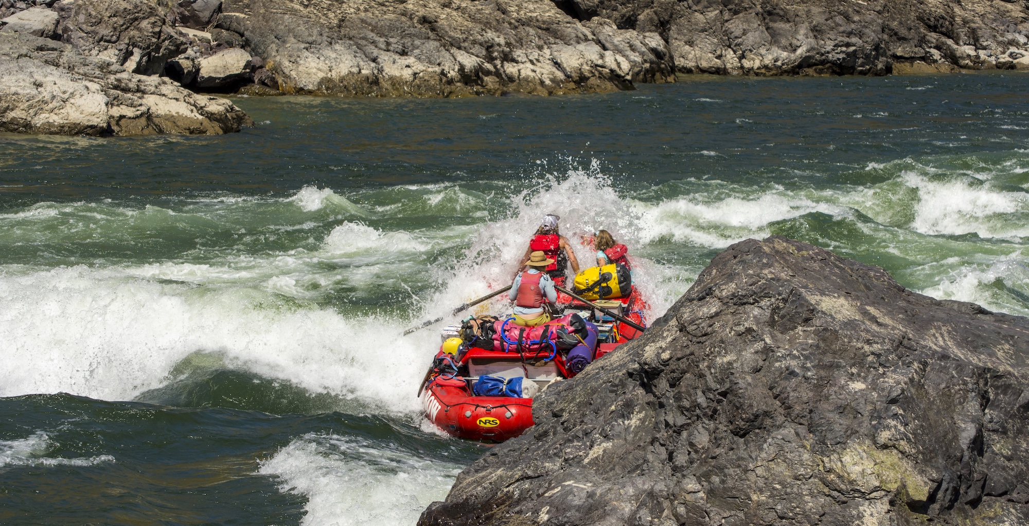 Red raft with people in it going through a splashy section of whitewater in Idaho.