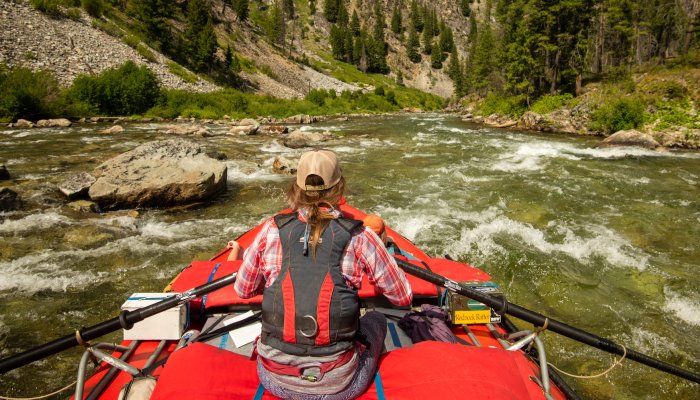 oar boat on wilderness river with green water, trees and rocks