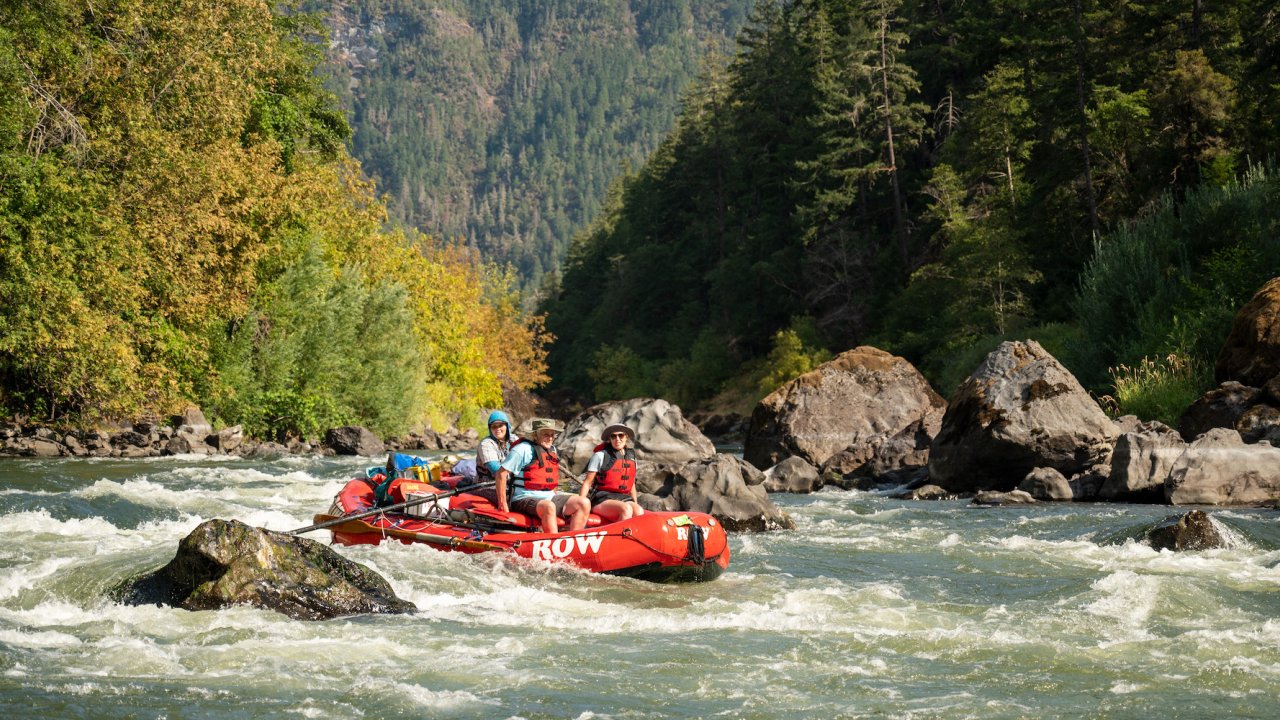 A red raft navigating through boulders in a river on a sunny day