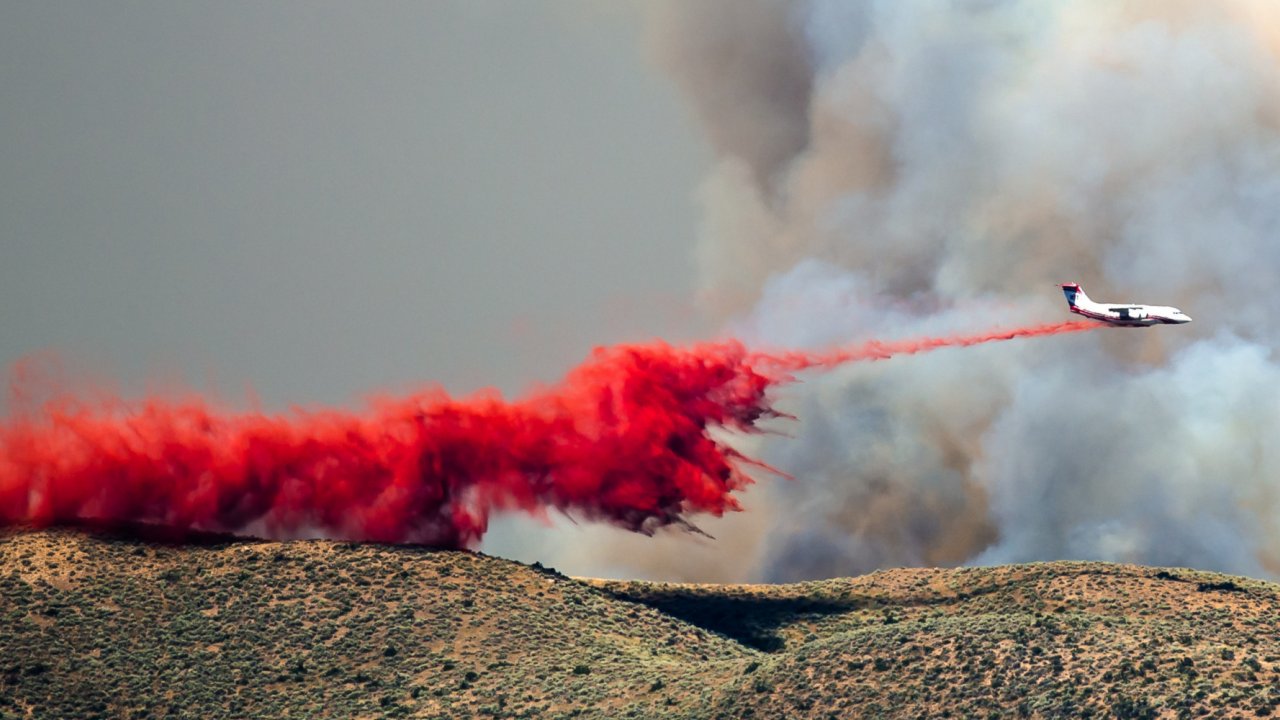 A plane dropping fire retardant on an active fire. The red color creates visibility of the retardant for air and ground crews. fire retardant being drop from plan