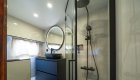 A yacht bathroom with a glass-enclosed rainfall shower, black vanity, and round mirror.