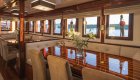 A yacht's indoor dining area with a polished wooden table, cushioned seating, and windows offering a view of the Adriatic Sea. 