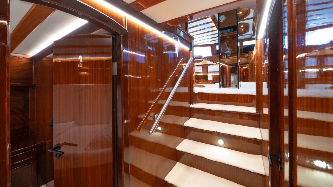 A glossy wooden staircase inside a yacht leading to the main deck.