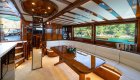 A yacht salon with polished wood interiors, long seating area, and large windows.
